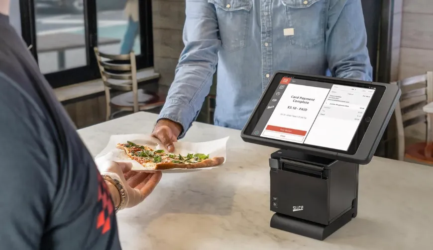 Customer receiving a slice of pizza at a modern point of sale with touchscreen interface.
