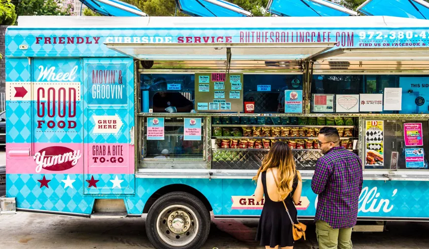 Two people order food at a vibrant food truck, illustrating a point of sale for curbside service with menus displayed.