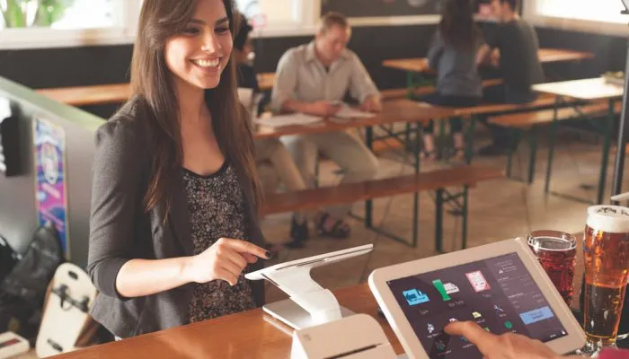 A woman making a purchase at a point of sale terminal in a café, with a touchscreen display and card reader.