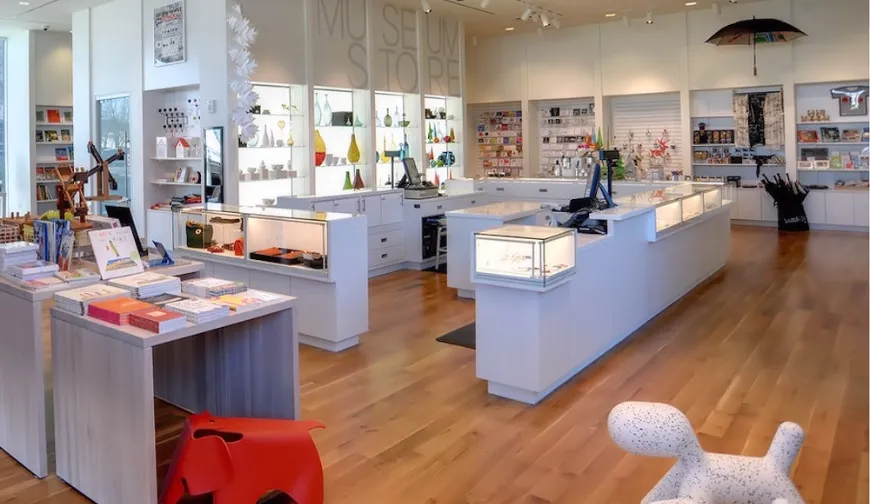 Modern museum store with wooden flooring, various display cases, and multiple point of sale stations.